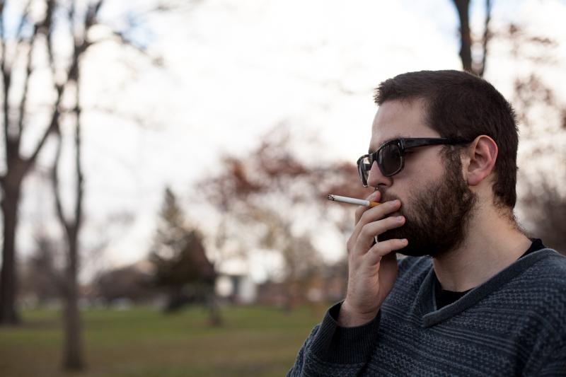College sophomore Carlos Armstrong smokes a cigarette in Tappan Square. The public park will become a designated smoking area for students after the College implements the tobacco-free policy on July 1, 2016.